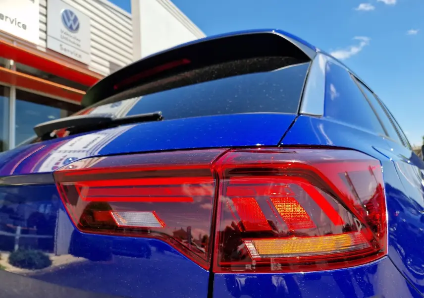 Feu arrière droit rouge et orange sur Volkswagen T-Roc bleu Lapiz, vue rapprochée du coin arrière sous un ciel bleu.