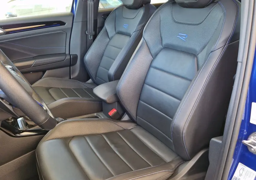 Vue intérieure côté conducteur du Volkswagen T-Roc bleu Lapiz 2022, sièges cuir noirs avec surpiqûres bleues et logo R brodé.