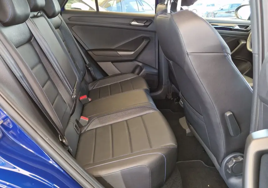 Vue intérieure côté gauche du Volkswagen T-Roc bleu Lapiz, montrant les sièges arrière en cuir noir avec surpiqûres bleues.