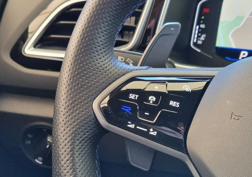 Gros plan sur le volant cuir perforé du Volkswagen T-Roc 2022, avec commandes de régulateur et logo R bleu illuminé.
