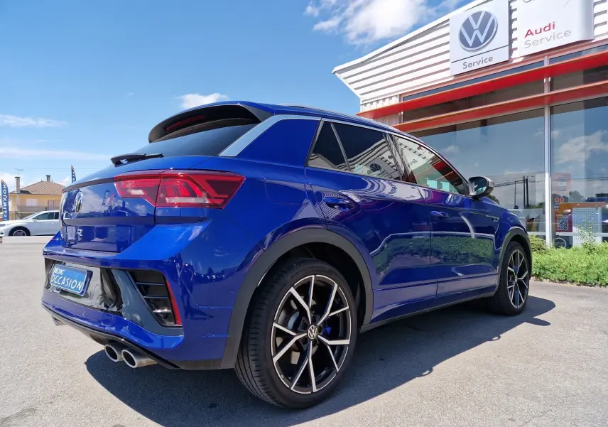 Volkswagen T-Roc bleu Lapiz vu en 3/4 arrière droit, avec jantes noires et doubles sorties d'échappement chromées.