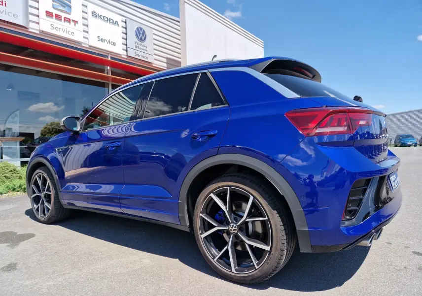 Volkswagen T-Roc bleu Lapiz en vue 3/4 arrière droit, jantes alliage noires et vitres teintées visibles.