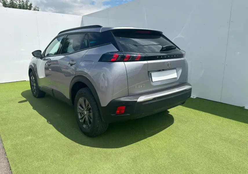 Vue 3/4 arrière droite du Peugeot 2008 gris clair avec feux arrière LED et barres de toit noires brillantes.
