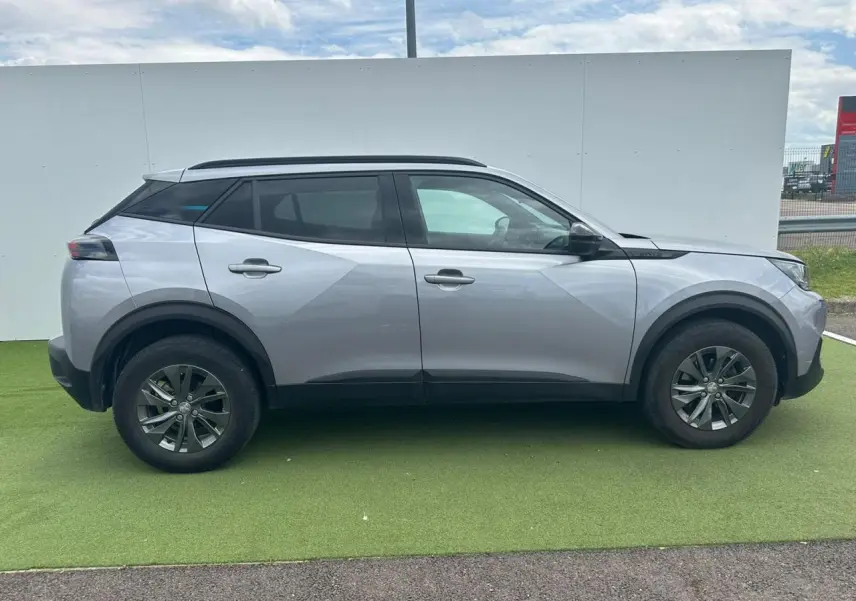 Peugeot 2008 gris clair vue de profil côté gauche, avec jantes alliage et barres de toit noires.