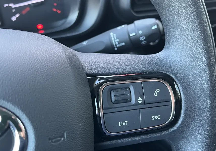 Gros plan sur les commandes au volant noir du Toyota Proace City blanc glacier, mettant en valeur les boutons de gestion audio et appel.