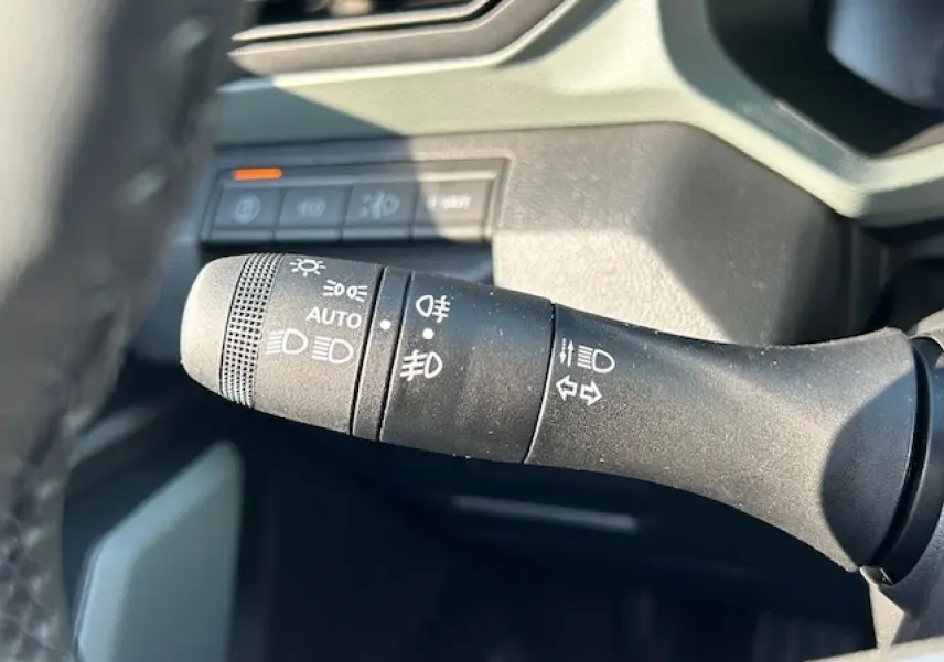 Gros plan sur la commande des phares et clignotants du Dacia Duster III 1.6 Hybrid 140, intérieur noir.