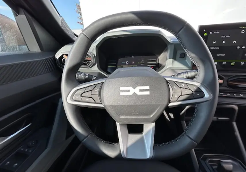 Vue intérieure centrée sur le volant noir du Dacia Duster III 1.6 Hybrid 140 4x2 Extreme avec tableau de bord digital.