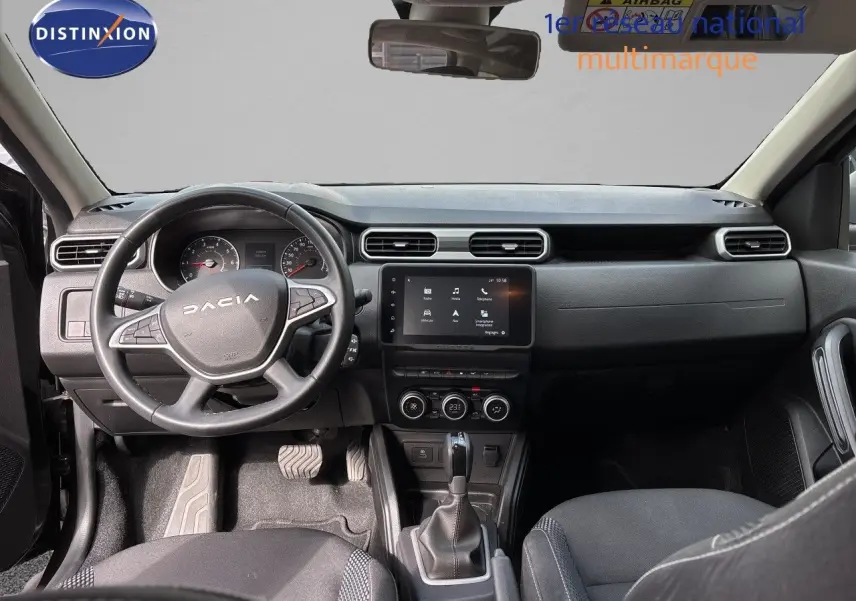 Vue intérieure côté conducteur du Dacia Duster 2024 noir, montrant le tableau de bord et les sièges en tissu noir.