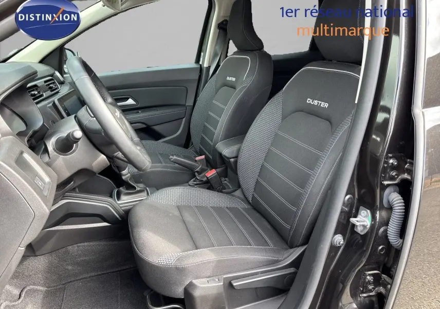 Vue intérieure côté conducteur du Dacia Duster noir 2024, mettant en valeur les sièges tissu noirs avec logo Duster brodé.
