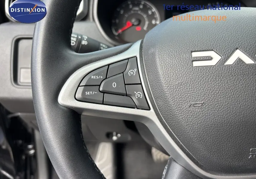 Gros plan sur le volant noir du Dacia Duster 2024 avec commandes intégrées côté gauche et logo partiel visible.