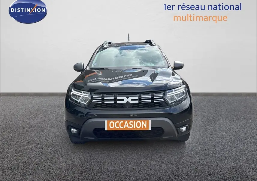 Vue avant du Dacia Duster noir 2024 avec calandre distinctive et phares LED allumés sur fond neutre.
