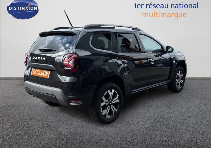 Dacia Duster noir en 3/4 arrière droit, avec jantes bi-ton et toit équipé de barres de toit.