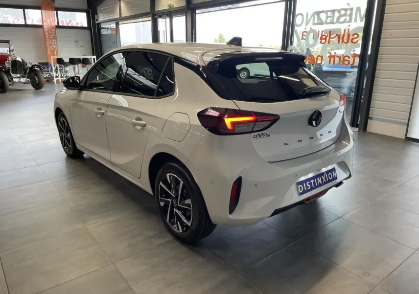 Opel Corsa blanche vue 3/4 arrière droit en intérieur, avec feux arrière LED allumés et jantes alliage noires.