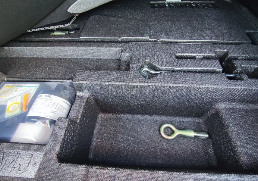 Compartiment de rangement dans le coffre de la Mazda MX-30 rouge métal 2023, avec outils et kit de réparation visibles.