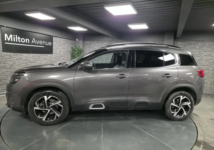 Vue profil côté gauche d'un Citroën C5 Aircross gris métallisé avec jantes alliage et barres de toit noires.