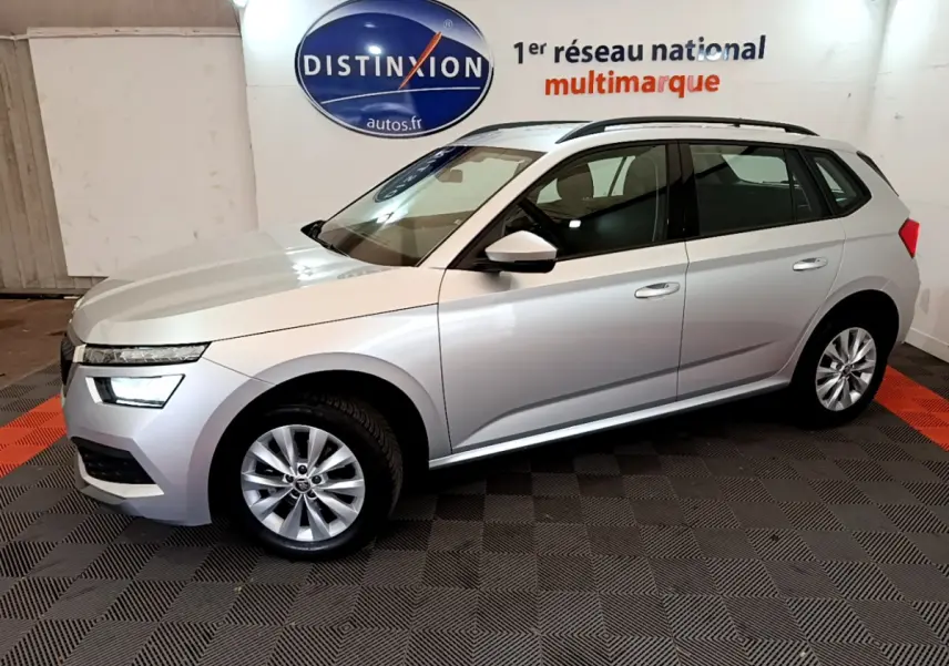 SKODA KAMIQ gris clair vu de profil côté gauche, intérieur showroom avec logo Distinxion en arrière-plan.