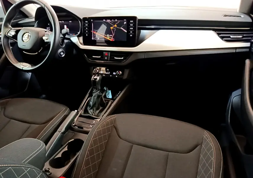 Intérieur du Skoda Kamiq 2022 vu de l'avant, sièges noirs avec surpiqûres, tableau de bord moderne et écran tactile central.
