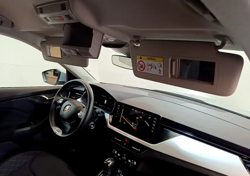 Intérieur du Skoda Kamiq 2022 vu côté conducteur, volant cuir et écran tactile de navigation allumé.