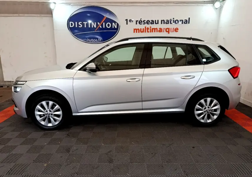 Vue de profil côté gauche d'un Skoda Kamiq gris clair 2022 avec jantes alliage et barres de toit noires.