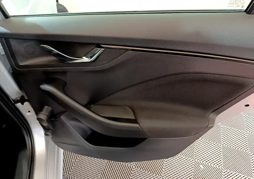 Gros plan sur la porte intérieure côté gauche du Skoda Kamiq gris clair, avec poignée chromée et panneau noir texturé.