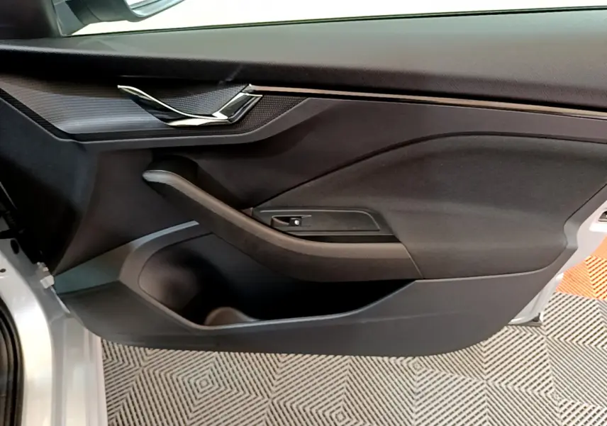 Gros plan sur la porte côté gauche intérieure du Skoda Kamiq gris clair, avec poignée chromée et panneau noir mat.