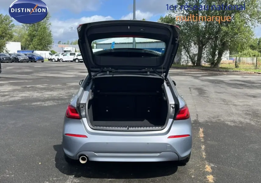 Vue arrière d'une BMW Série 1 116i 2022 en gris mat avec coffre ouvert sur un parking extérieur.