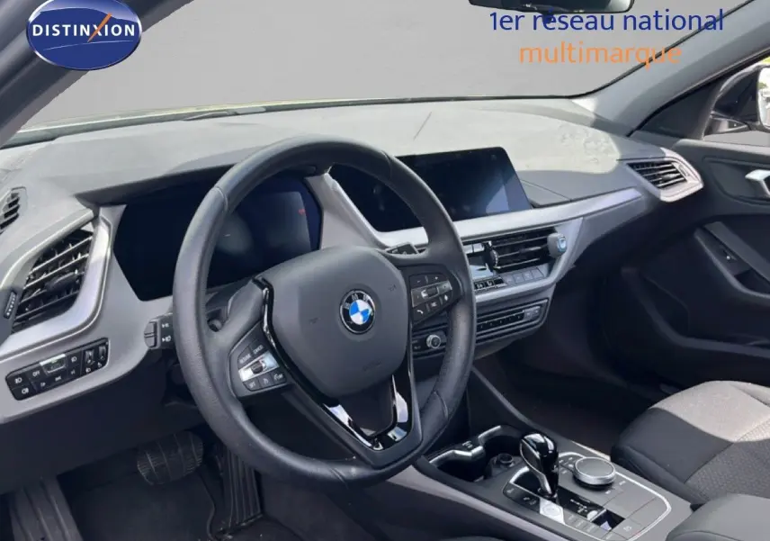 Vue intérieure côté conducteur de la BMW Série 1 116i 2022, volant cuir et tableau de bord moderne gris noir.