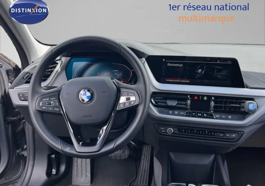 Vue intérieure centrée sur le volant BMW et le tableau de bord moderne avec écran tactile, ambiance gris noir.