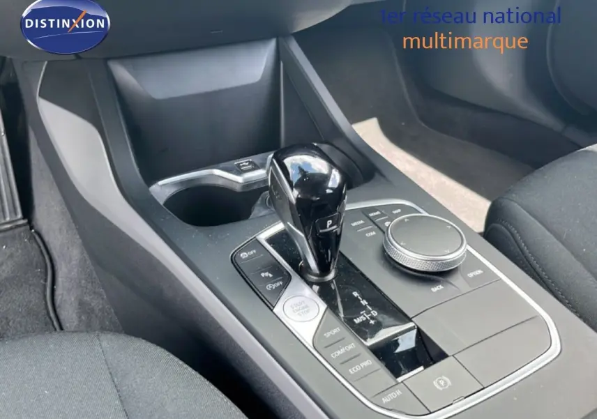 Gros plan sur la console centrale avec levier de vitesse et commandes, intérieur tissu gris de la BMW Série 1 116i 2022.