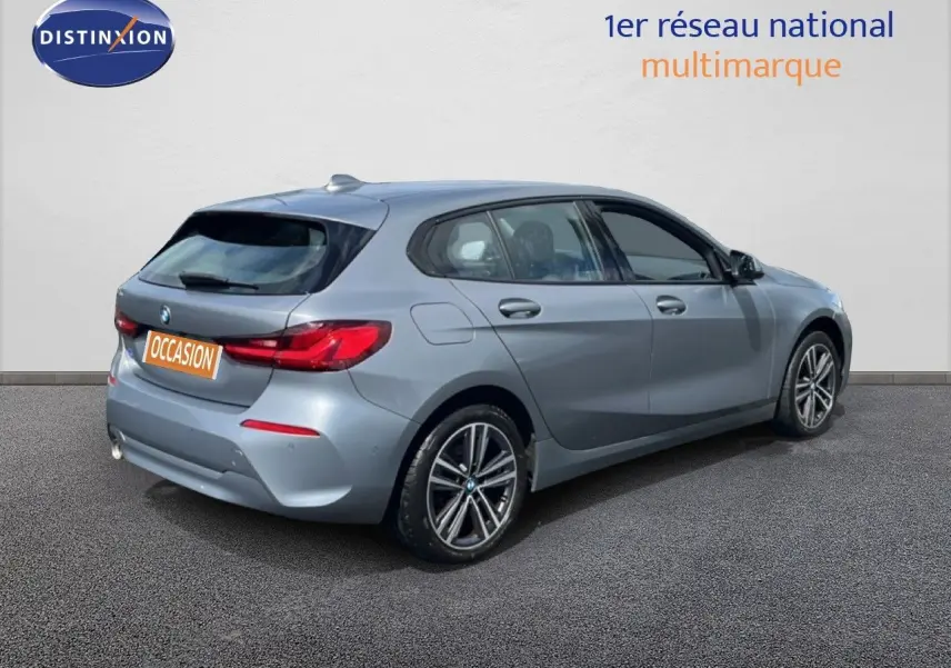 Vue 3/4 arrière droite d'une BMW Série 1 116i 2022 en gris mat Frozen Pure Grey avec jantes alliage bicolores.
