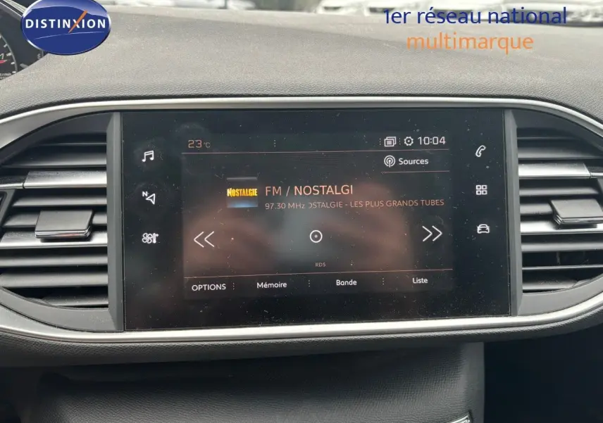 Écran tactile central du tableau de bord de la Peugeot 308 Bleu Magnetic affichant la radio FM Nostalgie à 10h04.