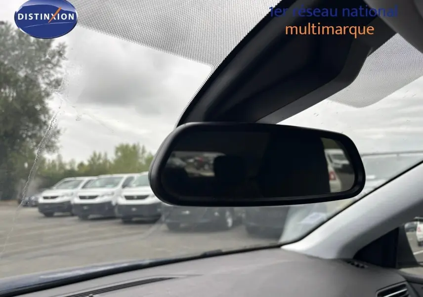 Vue intérieure du rétroviseur central d'une Peugeot 308 Bleu Magnetic, avec un parking en arrière-plan flou.