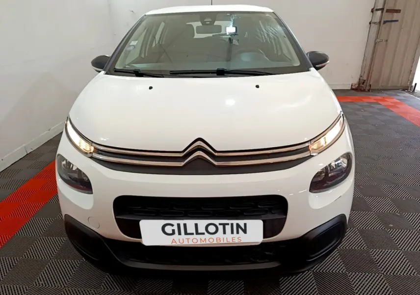 Vue avant d'une Citroën C3 blanche 2018 avec phares allumés et calandre noire dans un garage.