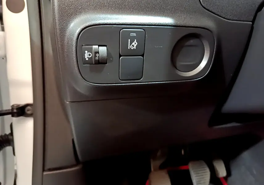 Vue rapprochée côté gauche du tableau de bord noir de la Citroën C3 blanche, avec commandes de réglage des phares et assistance.