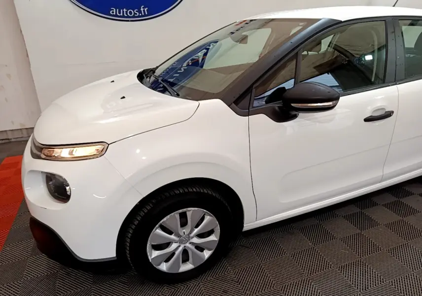 Vue 3/4 avant gauche d'une Citroën C3 blanche avec rétroviseur noir et feux avant allumés en intérieur.