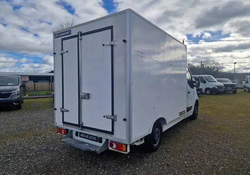 Vue 3/4 arrière droite d'un Renault Master blanc avec cellule frigorifique Lamberet et marchepied arrière sur terrain extérieur.