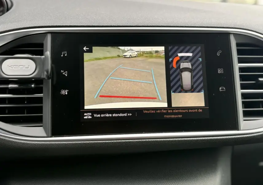 Écran tactile central affichant la caméra de recul et l'aide au stationnement de la Peugeot 308 blanche nacrée, vue intérieure.