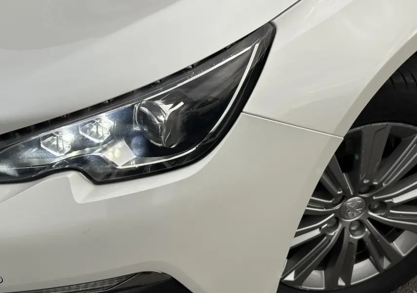 Gros plan sur le phare avant gauche et la jante alliage 16'' d'une Peugeot 308 blanc nacré de 2019.