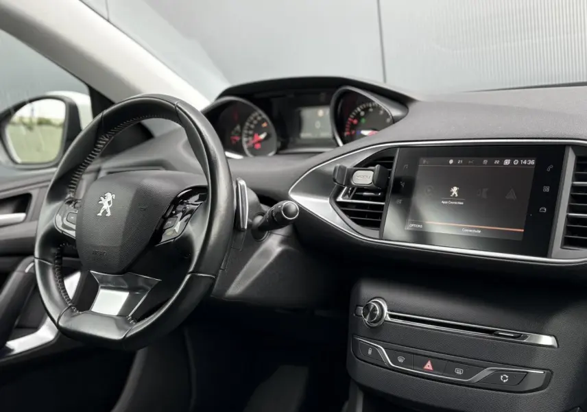 Intérieur de la Peugeot 308 blanc nacré, vue du tableau de bord avec volant cuir et écran tactile central.