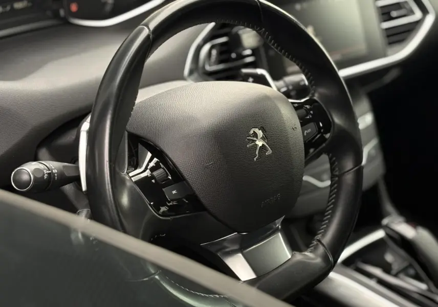 Gros plan sur le volant cuir noir multifonctions d'une Peugeot 308 1.2 PureTech 130 Allure, intérieur moderne.