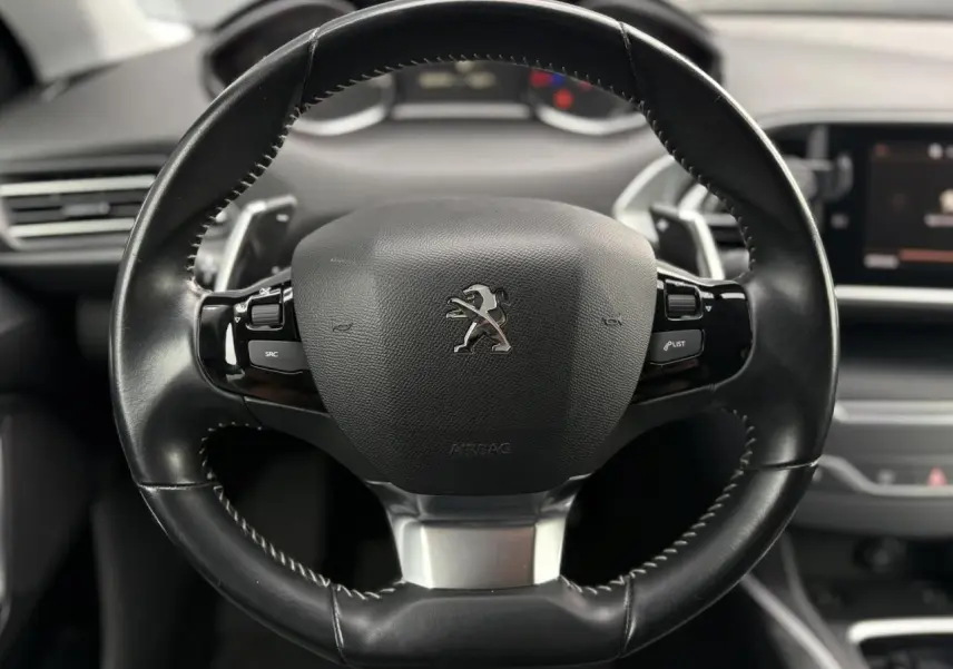 Volant sport en cuir noir avec logo Peugeot, vu de face dans l'habitacle d'une 308 blanche nacrée de 2019