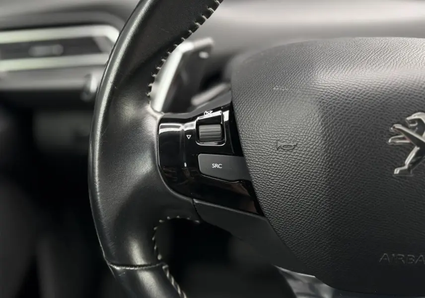 Gros plan sur le volant cuir noir de la Peugeot 308 2019 avec commandes intégrées et logo lion visible.