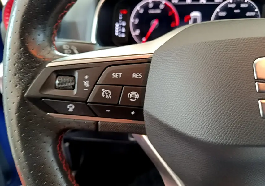 Gros plan sur le volant cuir noir avec commandes multifonctions du SEAT Arona bleu 2022, tableau de bord numérique visible.