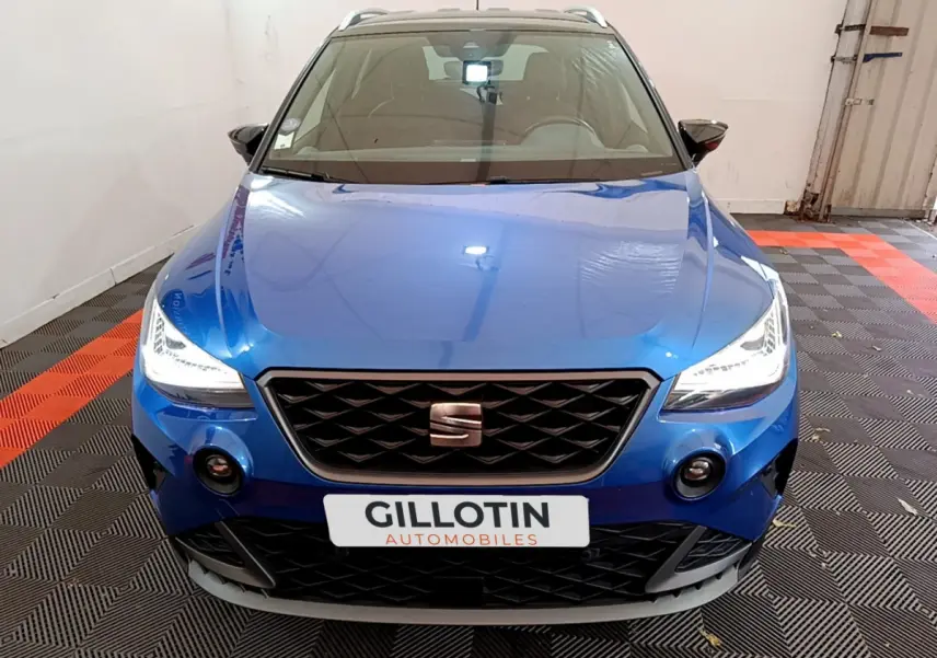 Vue frontale d'un SEAT Arona bleu 2022 avec phares LED allumés et calandre noire distinctive.