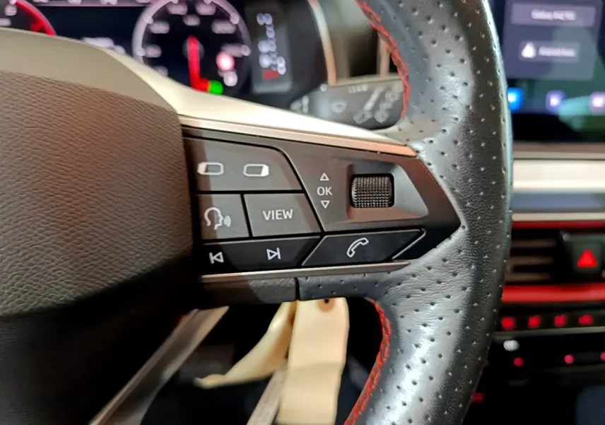 Gros plan sur les commandes du volant en cuir noir perforé avec surpiqûres rouges du SEAT Arona 2022.