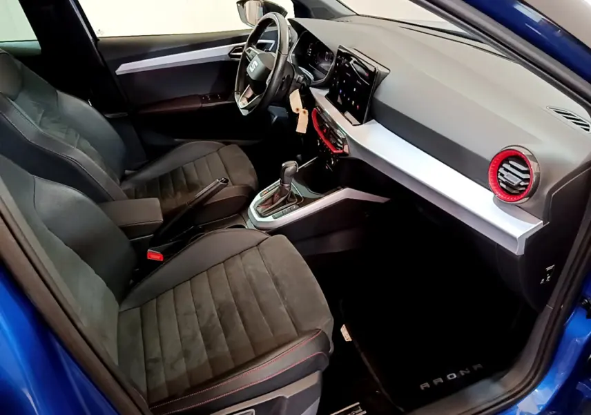 Intérieur avant droit du SEAT Arona bleu 2022, sièges noirs, volant cuir, tableau de bord avec écran tactile et aérateurs rouges.