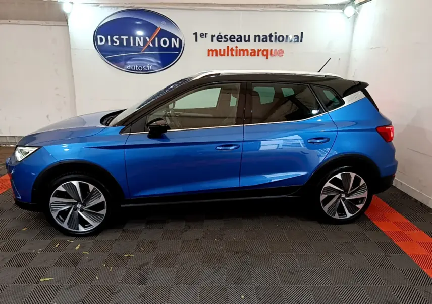 Profil côté gauche d'un SEAT Arona bleu 2022 avec toit noir et jantes alliage distinctives en intérieur showroom.