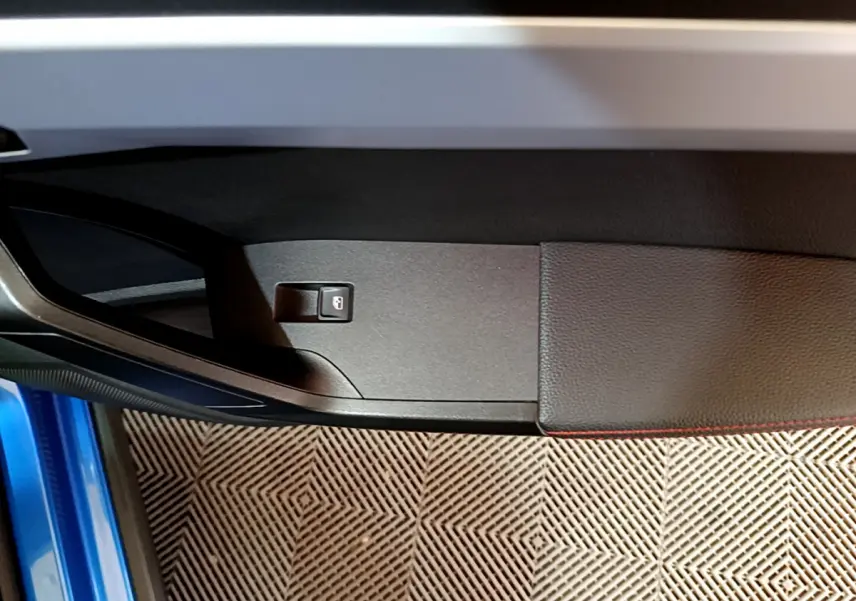 Détail de la porte côté gauche du SEAT Arona bleu 2022 avec bouton de verrouillage intégré et surpiqûres rouges.