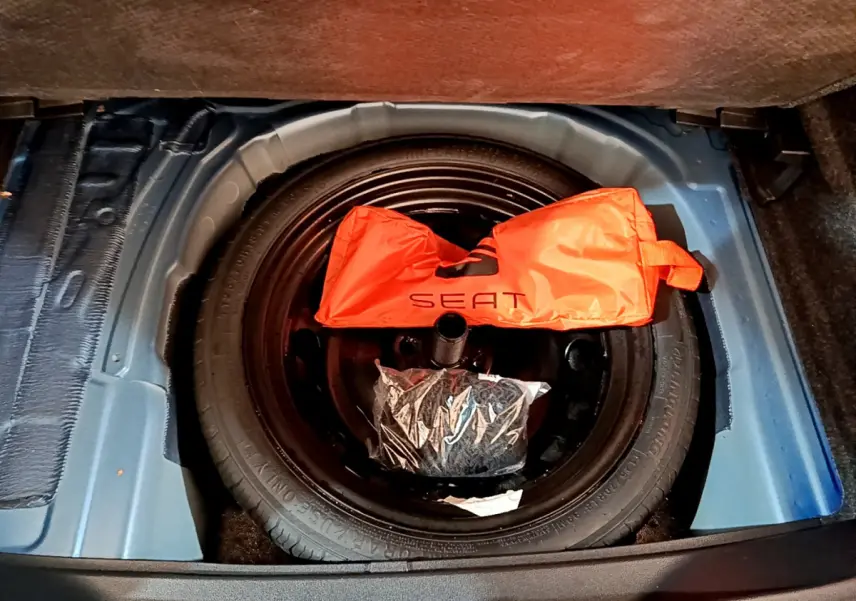 Vue plongeante sur la roue de secours noire dans le coffre bleu du SEAT Arona avec sac orange marqué SEAT.