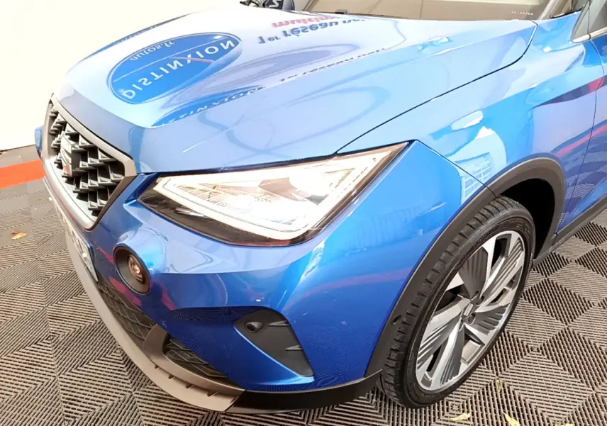Vue rapprochée 3/4 avant droit du SEAT ARONA bleu 2022, mettant en valeur le phare LED et la calandre distinctive.